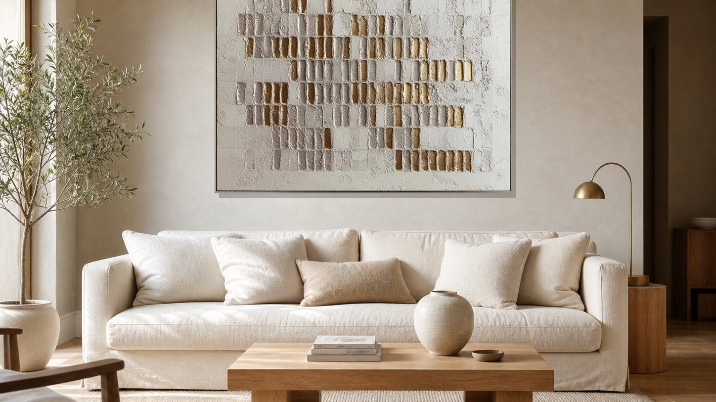 White and gold textured wall art above an ivory sofa in a warm neutral living room