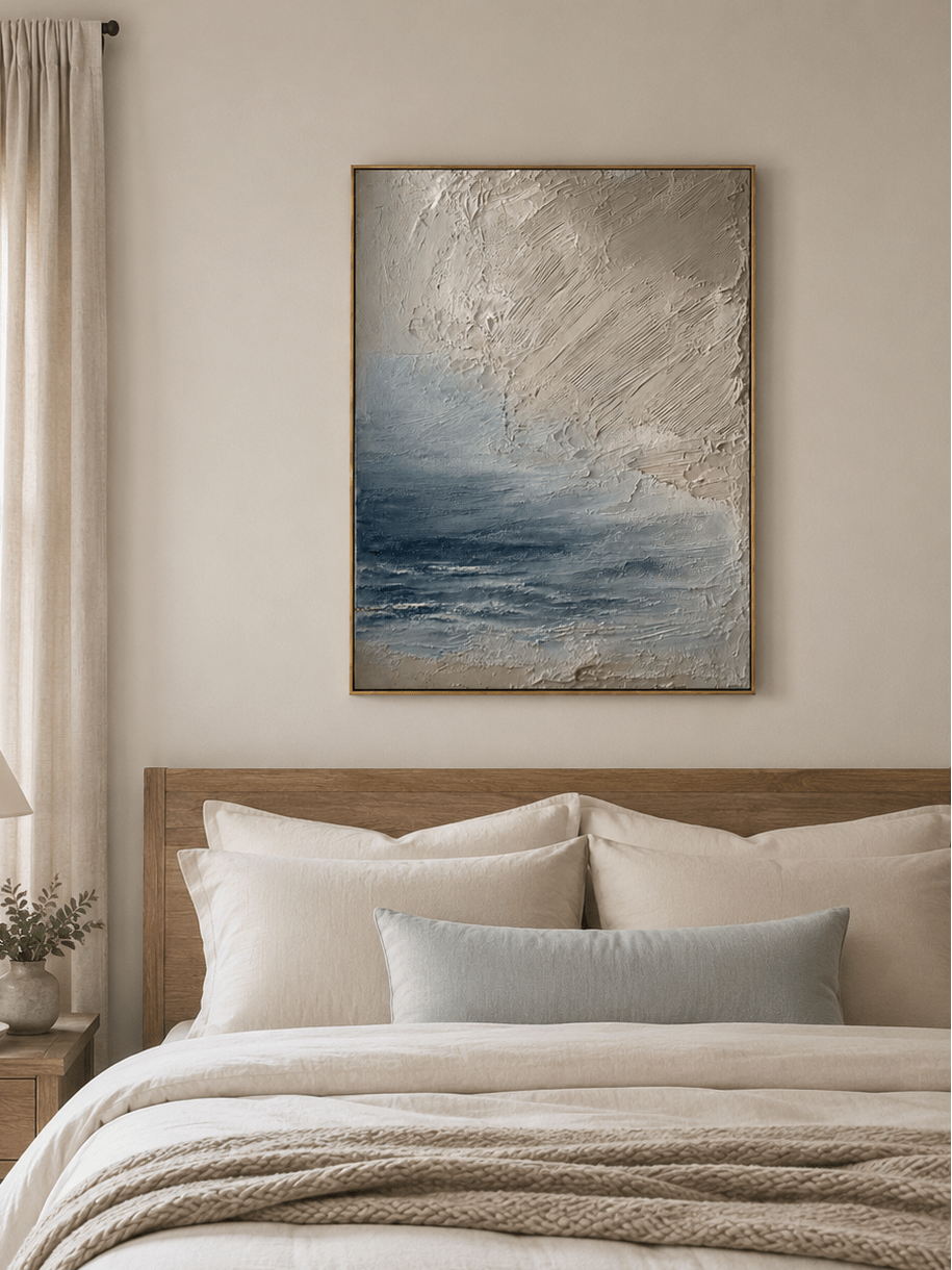 Blue-gray seascape painting displayed above the bed in a calm neutral bedroom