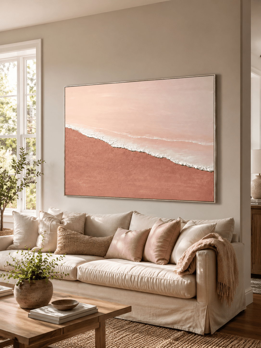 Blush pink coastal wall art displayed above a cream sofa in a soft contemporary living room