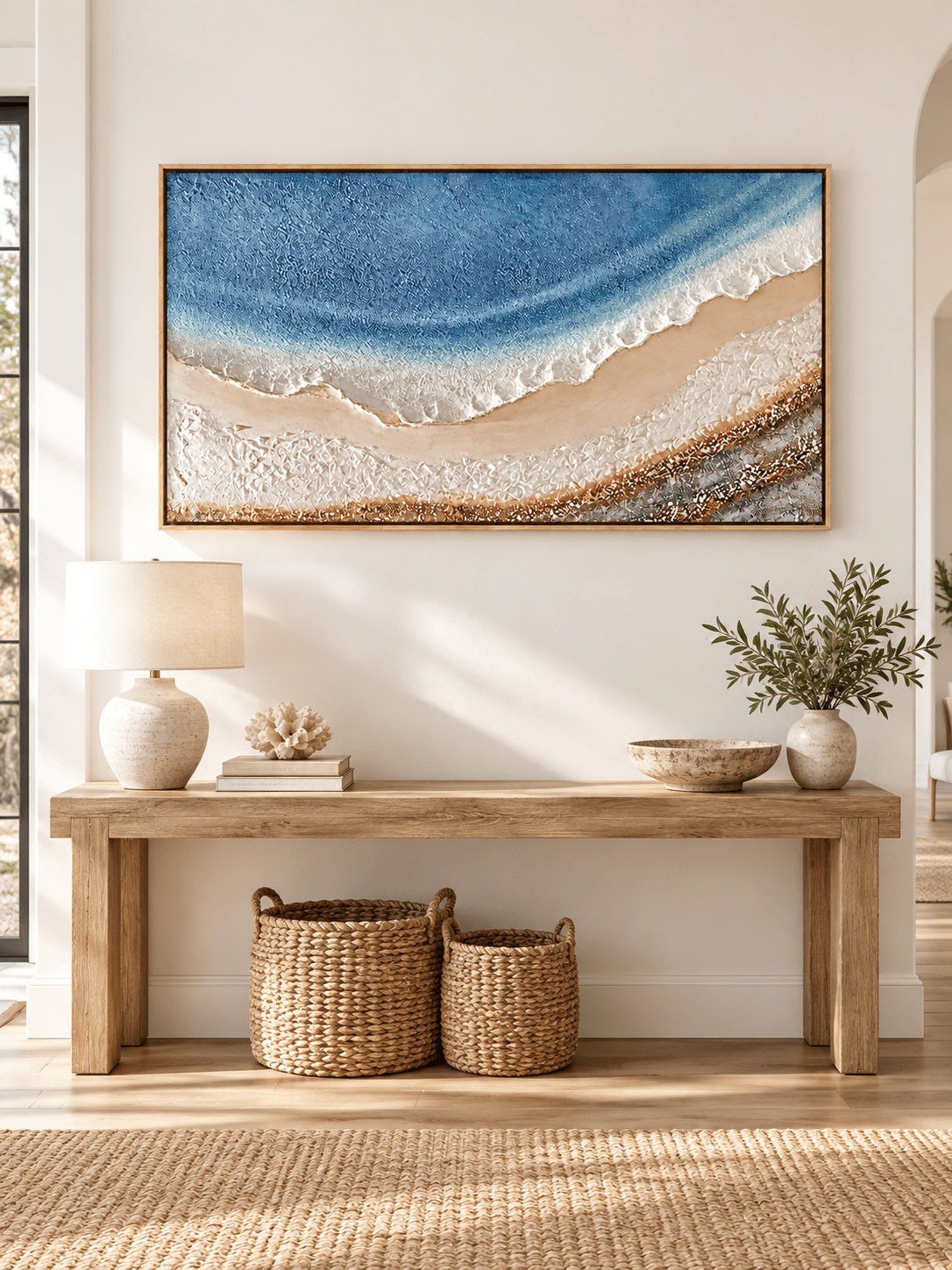 Horizontal blue ocean and sandy beach painting displayed above a console in a modern coastal entryway