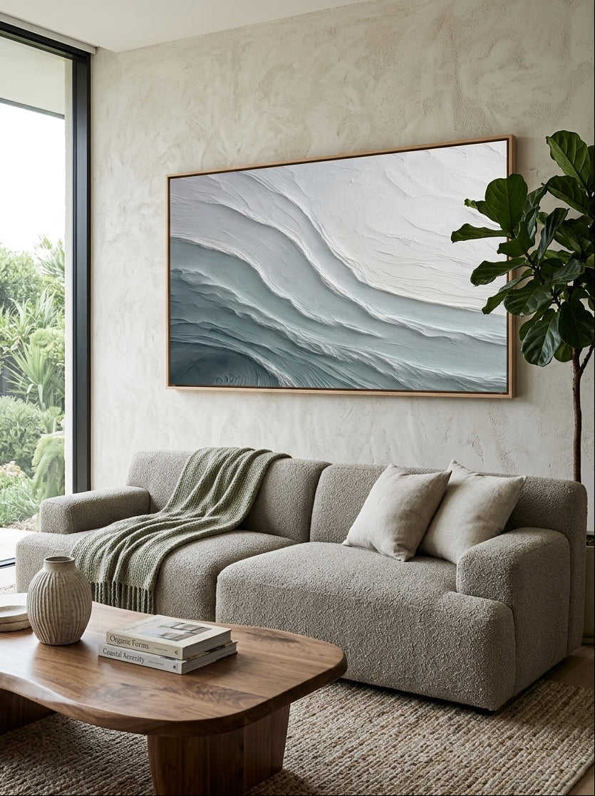 Oversized horizontal blue and white ocean wave canvas painting mounted above modern living room sofa