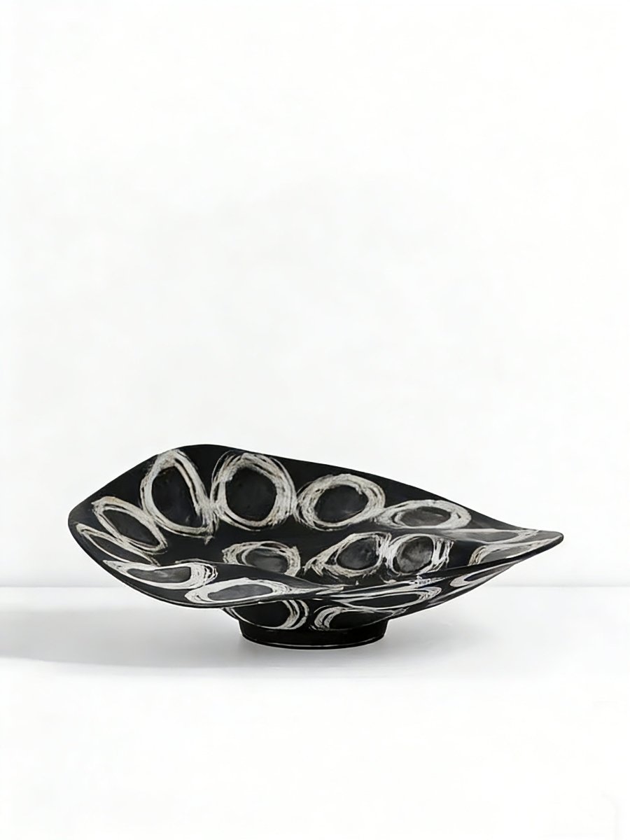 abstract black and white ceramic bowl with organic wavy edges and hand-painted circular patterns on a white console.