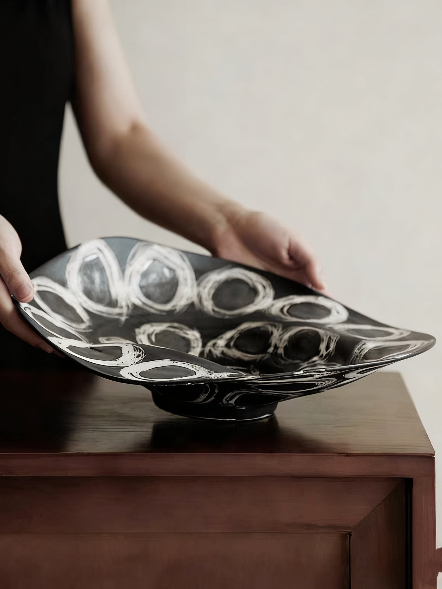 abstract black and white ceramic bowl with organic wavy edges and hand-painted circular patterns on a white console.