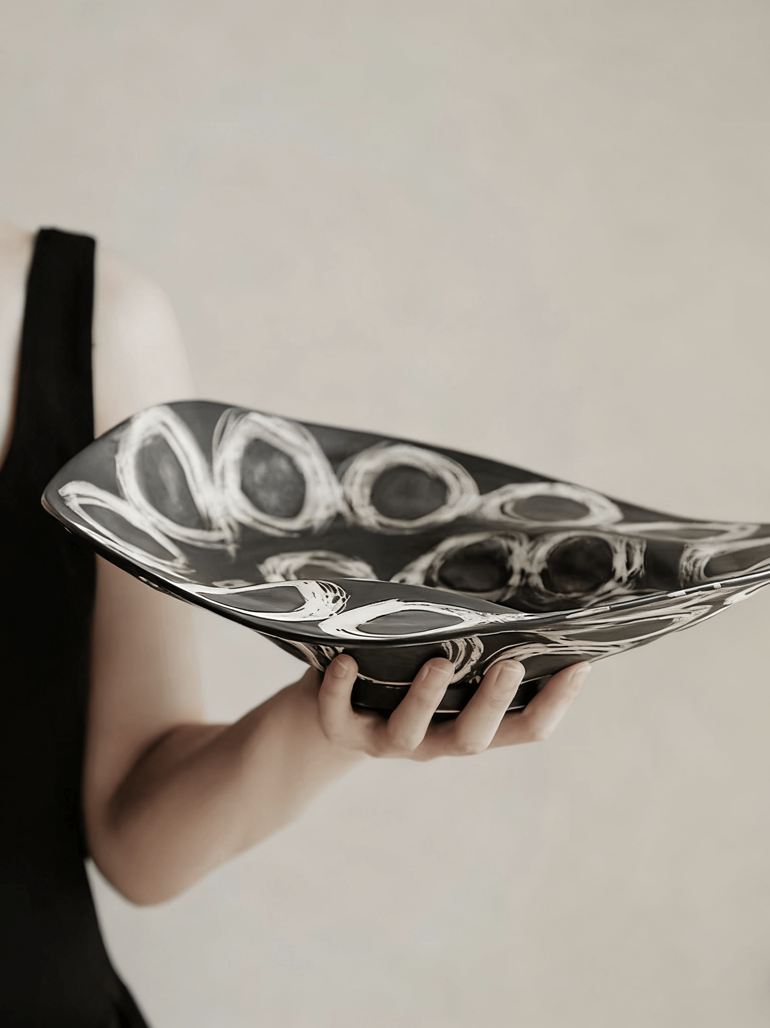 abstract black and white ceramic bowl with organic wavy edges and hand-painted circular patterns on a white console.