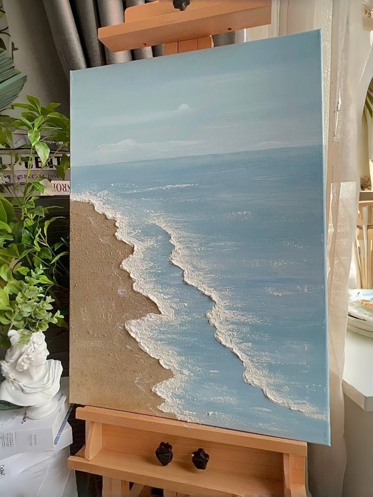 Large vertical hand-painted blue ocean painting with 3D textured white foam waves and sandy beach by Leo Liang in a bright modern bedroom.