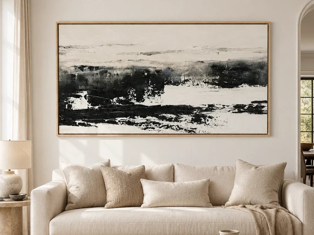 Wide black and white abstract landscape painting above a cream sofa in a neutral living room.