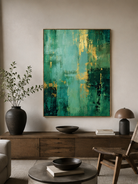 Emerald green and gold abstract painting displayed above neutral furniture in a contemporary living room
