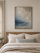 Blue-gray seascape painting displayed above the bed in a calm neutral bedroom