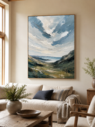 Sage green coastal landscape painting above a cream sofa in an organic modern living room