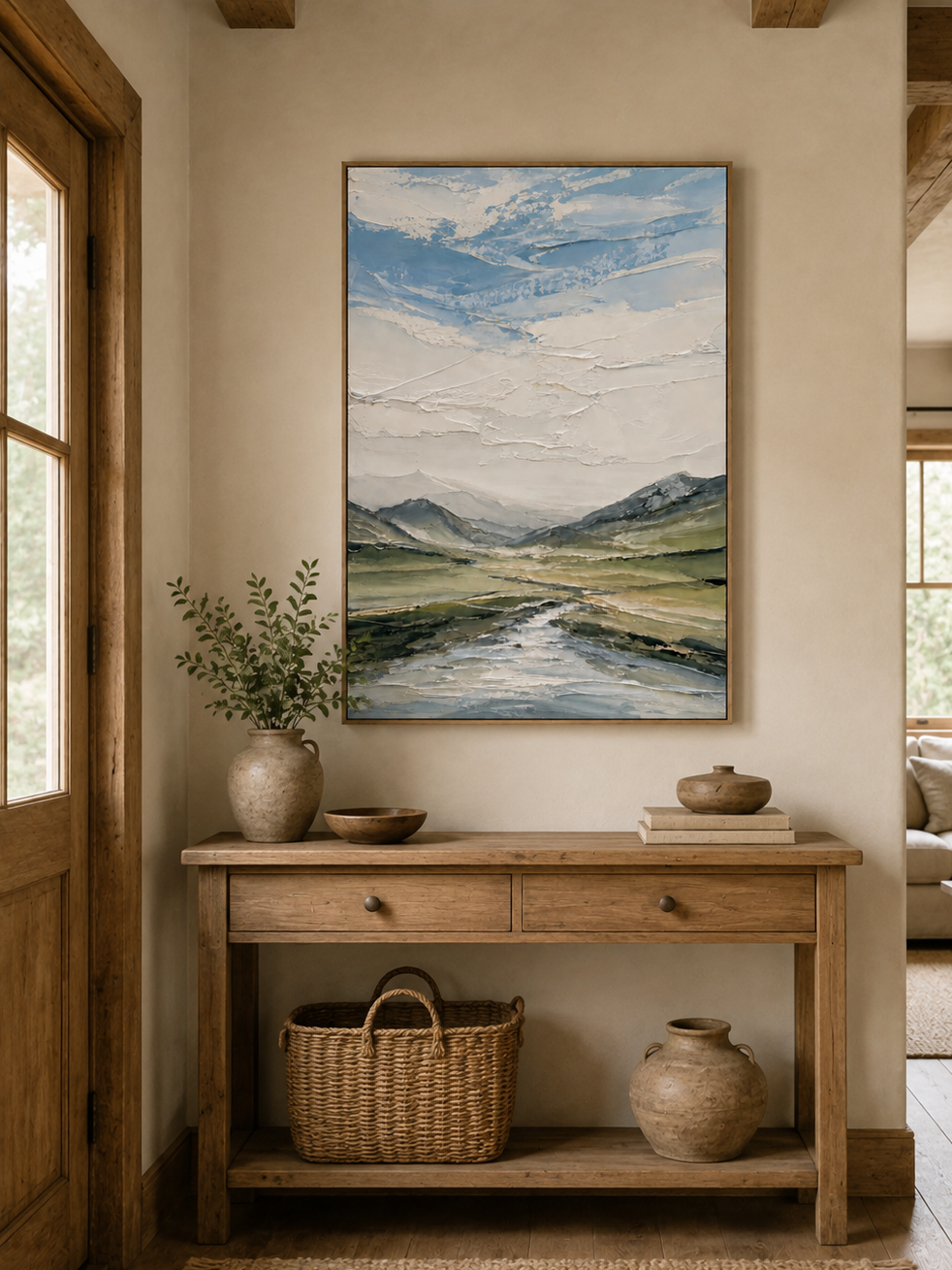 Textured mountain and river landscape painting displayed above a wood console in a modern neutral entryway