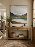 Sage green mountain lake painting displayed above a wood console in an organic modern entryway