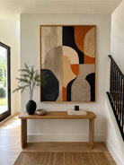Terracotta and black abstract painting displayed above a wood console in an organic modern entryway