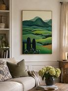 Green rolling hills landscape painting displayed above neutral furniture in an organic modern living room