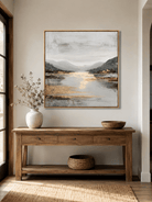 Gray and gold mountain lake wall art displayed above an entryway console in a contemporary neutral home