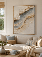 Textured ocean shoreline painting above a cream sofa in an organic modern living room