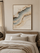 Neutral blue and ivory coastal wall art displayed above a bed in a calm modern bedroom