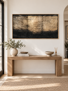 Extra wide black and gold-toned abstract wall art displayed above a long entryway console in an organic modern interior