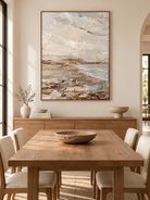 Vertical neutral coastal landscape wall art displayed in an open dining room with natural wood and stone furniture