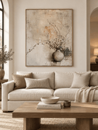 Large neutral botanical vase wall art displayed above a sofa in a warm modern organic living room
