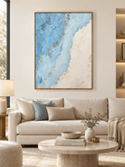 Large blue and white textured coastal wall art displayed above a sofa in a modern neutral living room