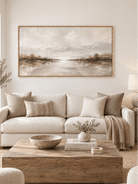 Large neutral panoramic lake landscape painting displayed above a sofa in a modern organic living room