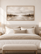 Peaceful misty lake painting displayed above a bed in a warm minimalist bedroom
