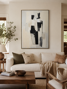 Black and beige abstract figures painting above a neutral sofa in a minimalist living room