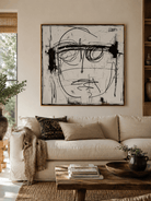 Black and white abstract face painting above a neutral sofa in a contemporary living room
