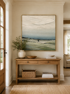 Neutral sage green landscape painting displayed above a wood console in an organic modern entryway