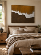 Earth tone coastal wall art displayed above the bed in a warm neutral modern bedroom