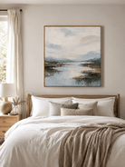 Soft blue mountain river landscape painting displayed above the bed in a warm neutral bedroom