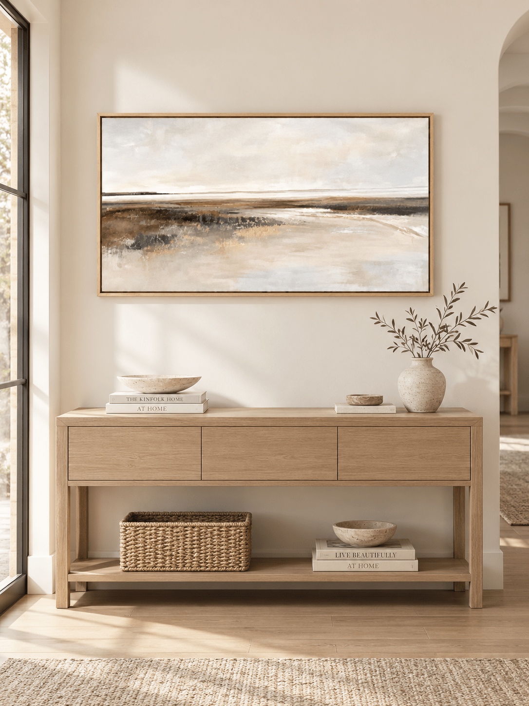 Wide neutral abstract shoreline painting displayed above a long console in a minimalist entryway