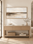 Wide neutral abstract shoreline painting displayed above a long console in a minimalist entryway
