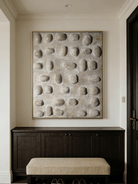 Close-up of hand-painted 3D relief wall art, featuring raised oval stone-like textures in warm beige plaster on a large canvas for a minimalist bedroom.