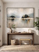 Calming misty mountain and lake artwork displayed above console table in minimalist entryway hallway