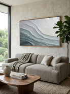 Oversized horizontal blue and white ocean wave canvas painting mounted above modern living room sofa
