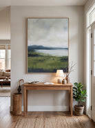 Framed textured green landscape painting styled above a natural wood console table in a bright entryway