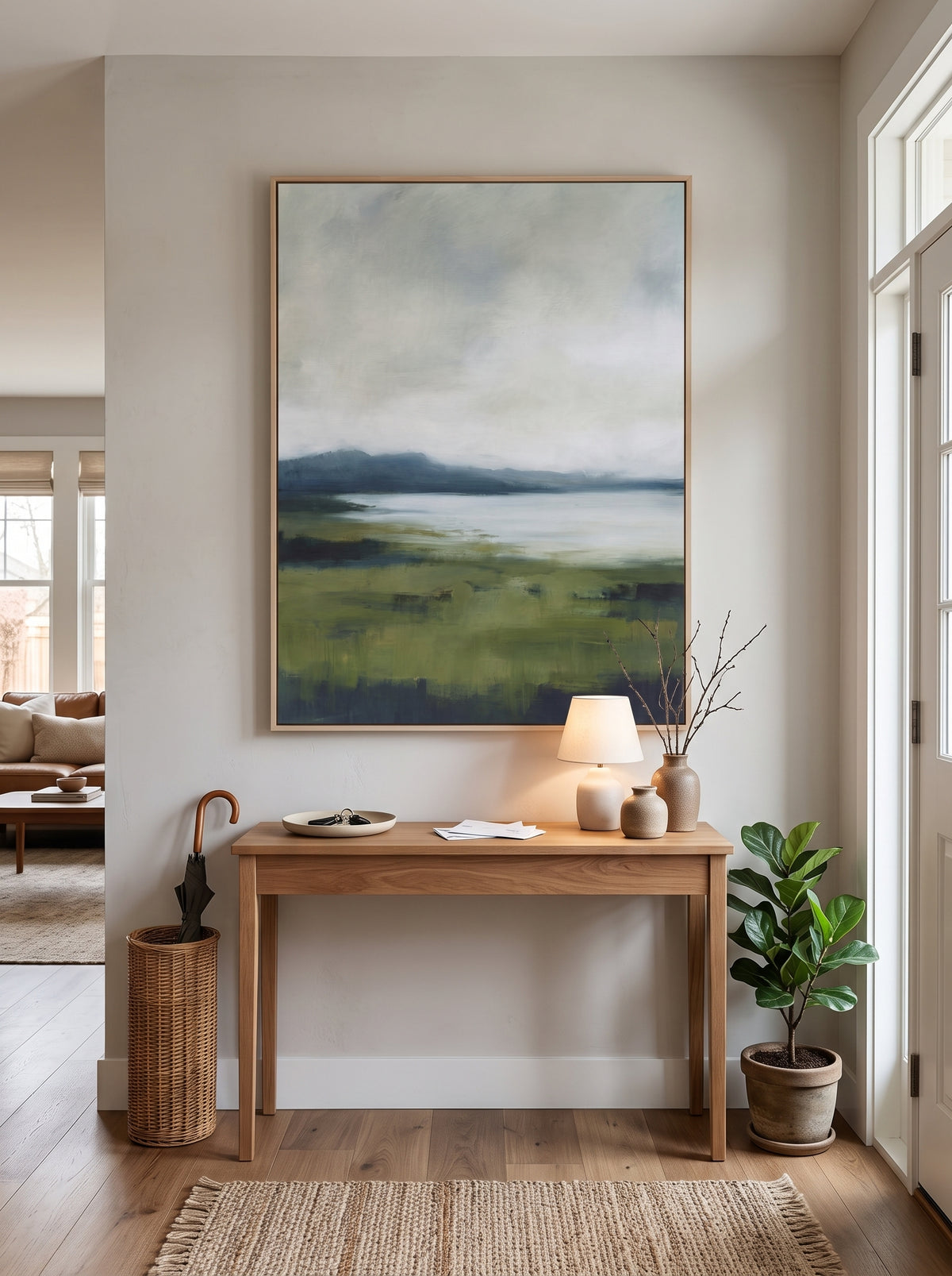 Framed textured green landscape painting styled above a natural wood console table in a bright entryway