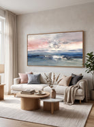 Abstract coastal seascape painting with blush pink and blue tones displayed above a sofa in a modern living room.