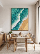 Framed aerial beach and ocean wave oil painting displayed in airy dining room with light oak furniture