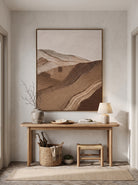 Sculptural earthy brown wave relief canvas painting hung above minimalist console table in Japandi foyer