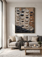 Large vertical earth-tone 3D stone relief canvas artwork displayed next to modern neutral sofa in minimalist living room