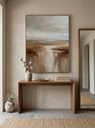 Framed textured earthy horizon painting styled above a wooden console table in a modern entryway