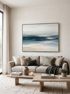 Large horizontal deep teal abstract ocean canvas wall art above modern neutral sofa in living room