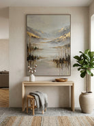 Framed textured misty mountain painting placed over a modern wooden console table in a bright entryway