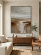 Vertical textured brown and beige abstract landscape painting mounted above a modern neutral sofa