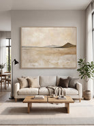 Oversized horizontal warm beige and sand mountain landscape painting mounted above a modern neutral sofa
