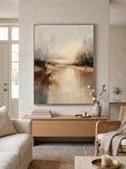 Vertical textured abstract lake landscape painting in warm neutral earth tones mounted above a living room sofa