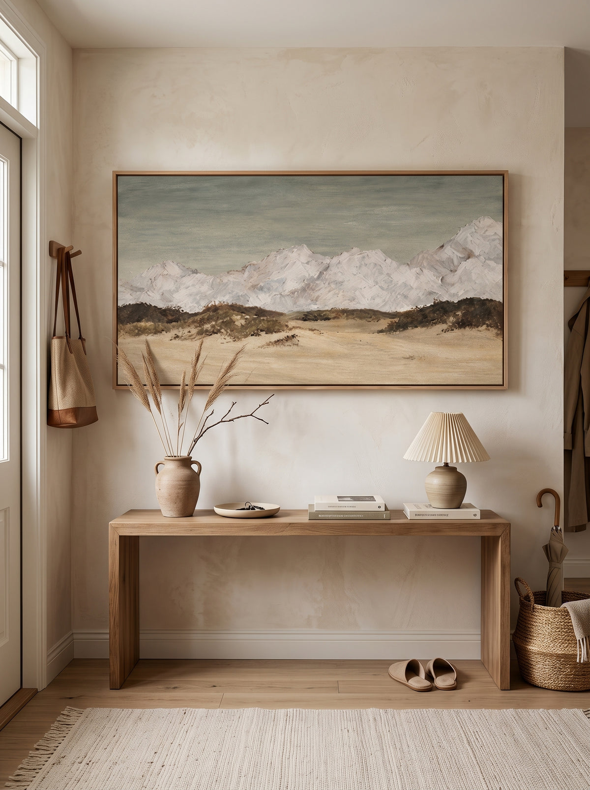 Textured minimalist mountain painting with snowy peaks displayed in a warm modern entryway with neutral decor.