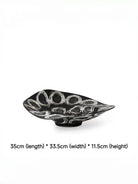 abstract black and white ceramic bowl with organic wavy edges and hand-painted circular patterns on a white console.